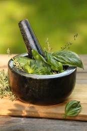 Photo of Fresh herbs. Basil leaves in mortar and thyme on wooden table outdoors, closeup