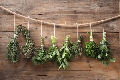 Photo of Bunches of different aromatic herbs hanging on rope near wooden wall