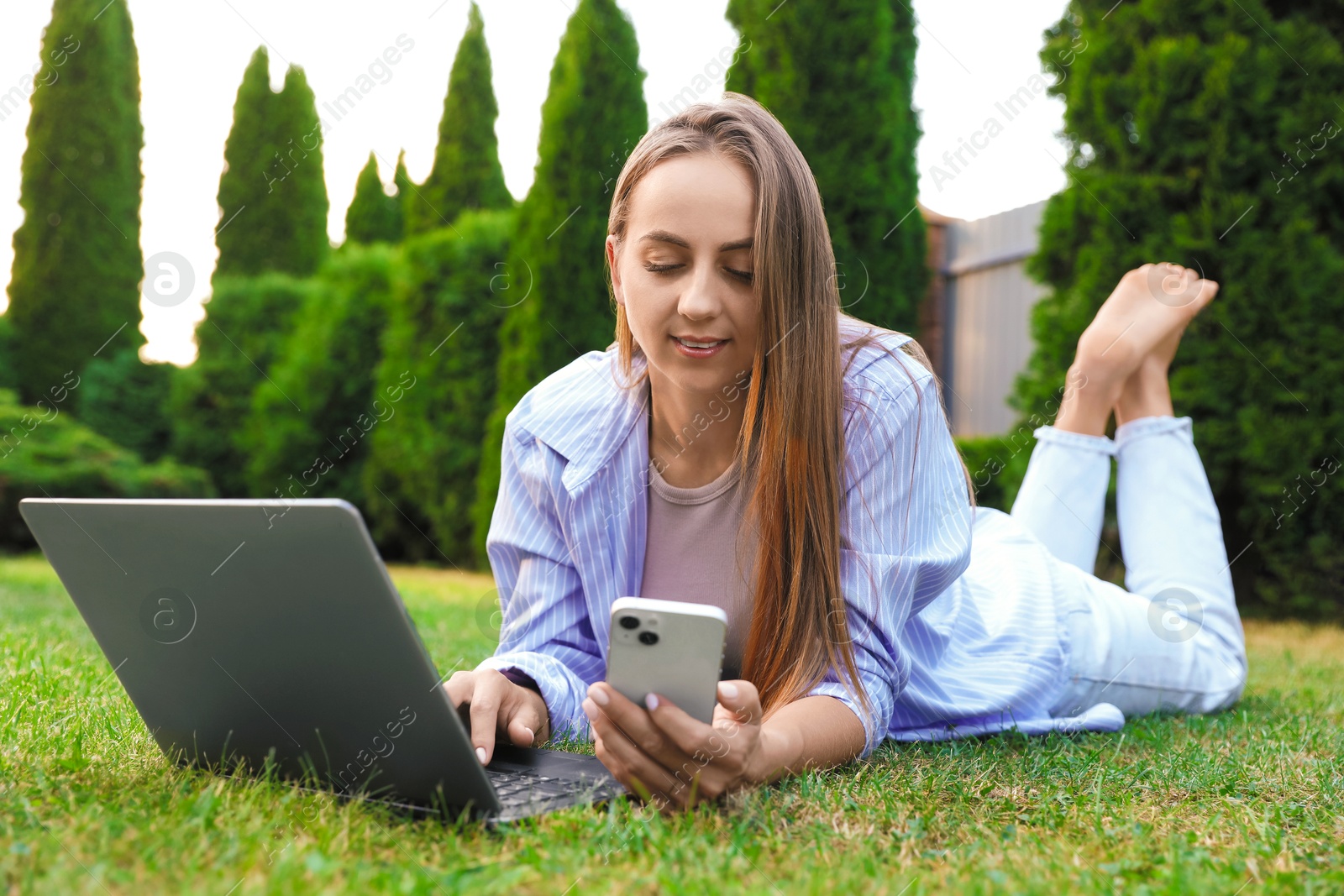 Photo of Woman with smartphone using laptop on green lawn in park