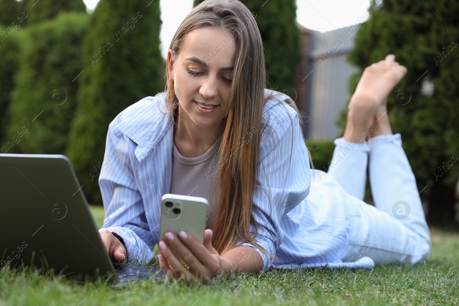 Photo of Woman with smartphone using laptop on green lawn in park