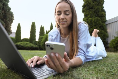 Photo of Woman with smartphone using laptop on green lawn in park