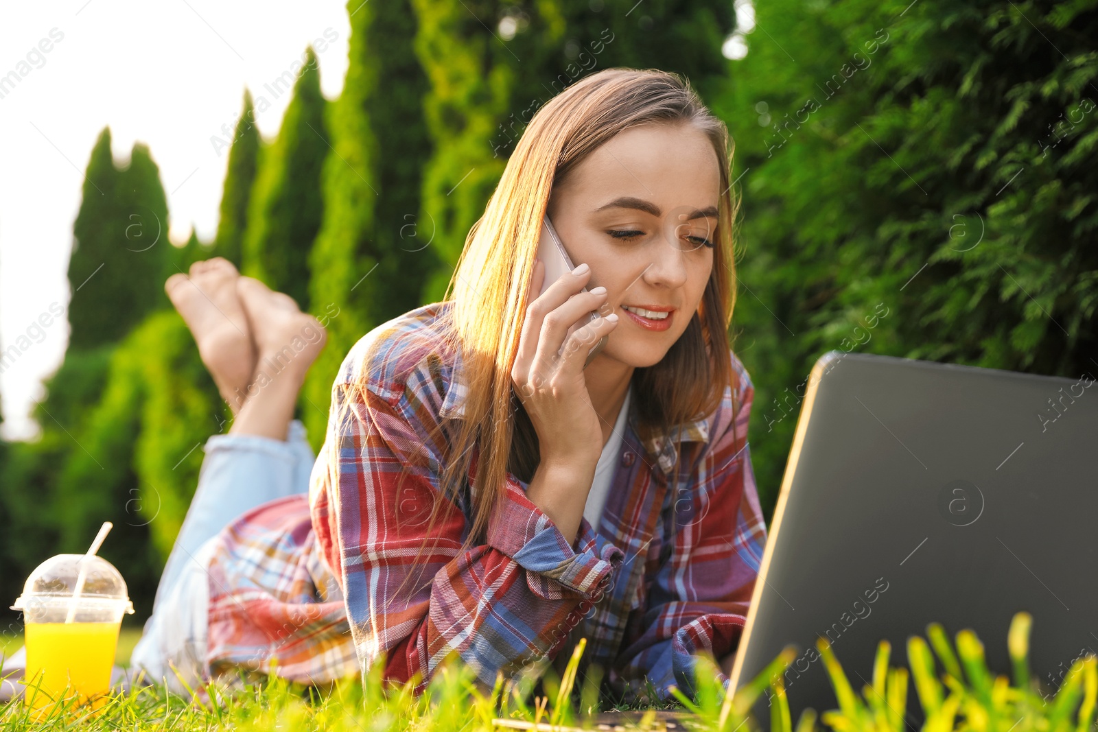 Photo of Woman talking on smartphone near laptop on green lawn in park