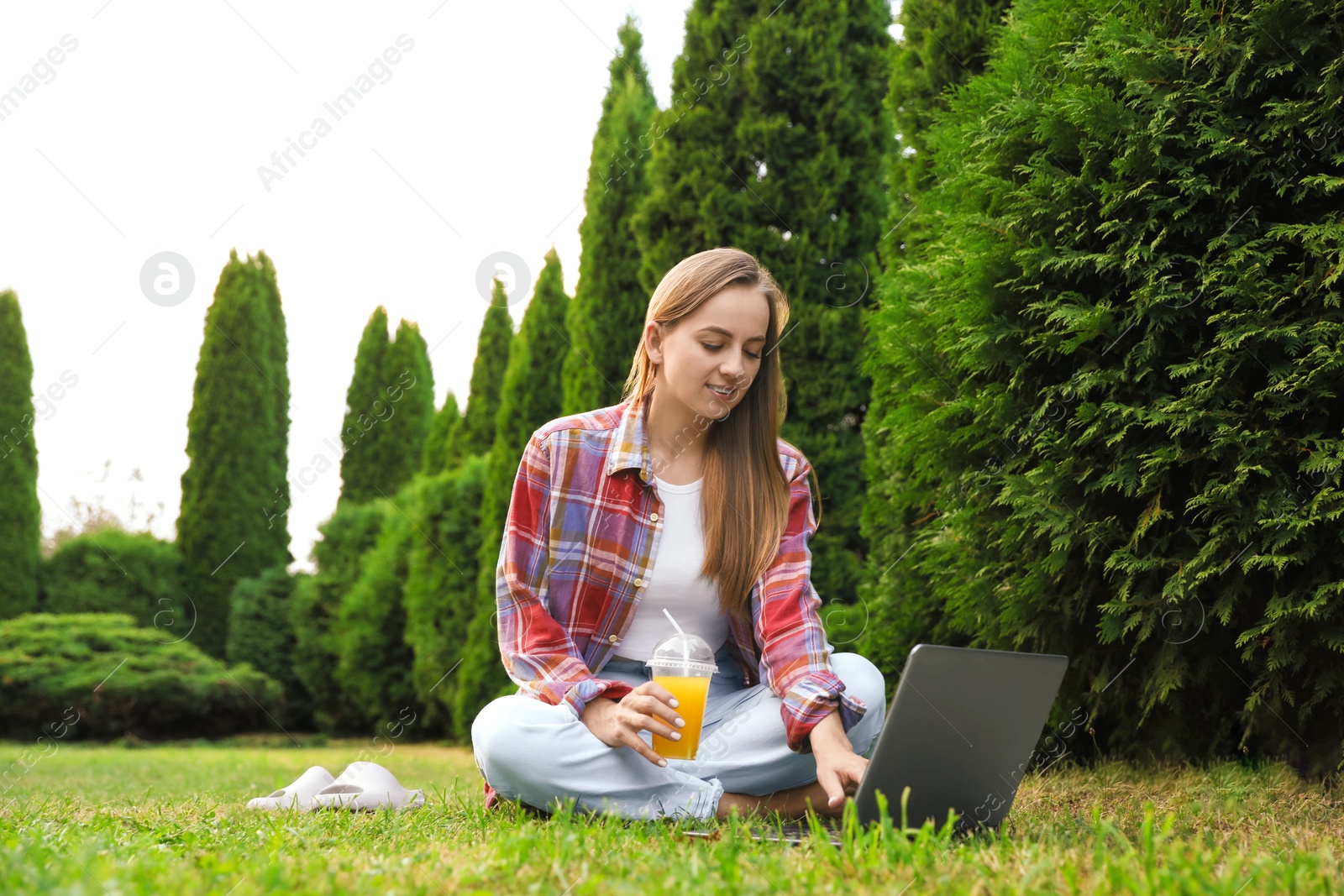 Photo of Woman with juice using laptop on green lawn in park