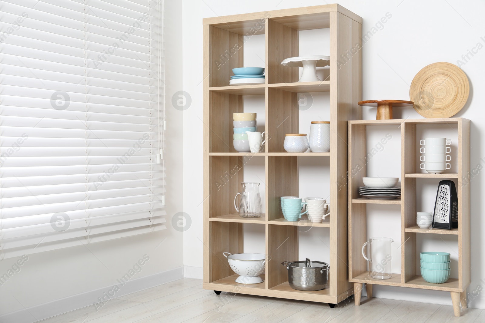 Photo of Wooden shelving units with kitchenware near white wall indoors