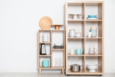 Photo of Wooden shelving units with kitchenware near white wall indoors