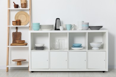 Photo of Storage stand and cabinet with kitchenware near white wall indoors