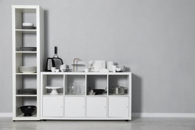 Shelving unit and storage cabinet with kitchenware near grey wall indoors