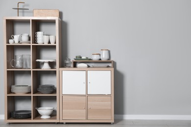 Wooden shelving unit and storage cabinet with kitchenware near grey wall indoors