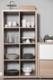 Photo of Wooden shelving unit and storage cabinet with kitchenware near grey wall indoors