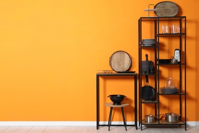 Photo of Storage stands with kitchenware near orange wall indoors