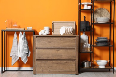 Storage stands and chest of drawers with kitchenware near orange wall indoors