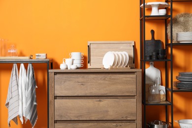 Photo of Storage stands and chest of drawers with kitchenware near orange wall indoors