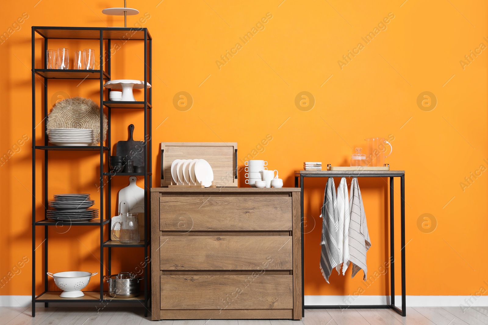 Photo of Storage stands and chest of drawers with kitchenware near orange wall indoors