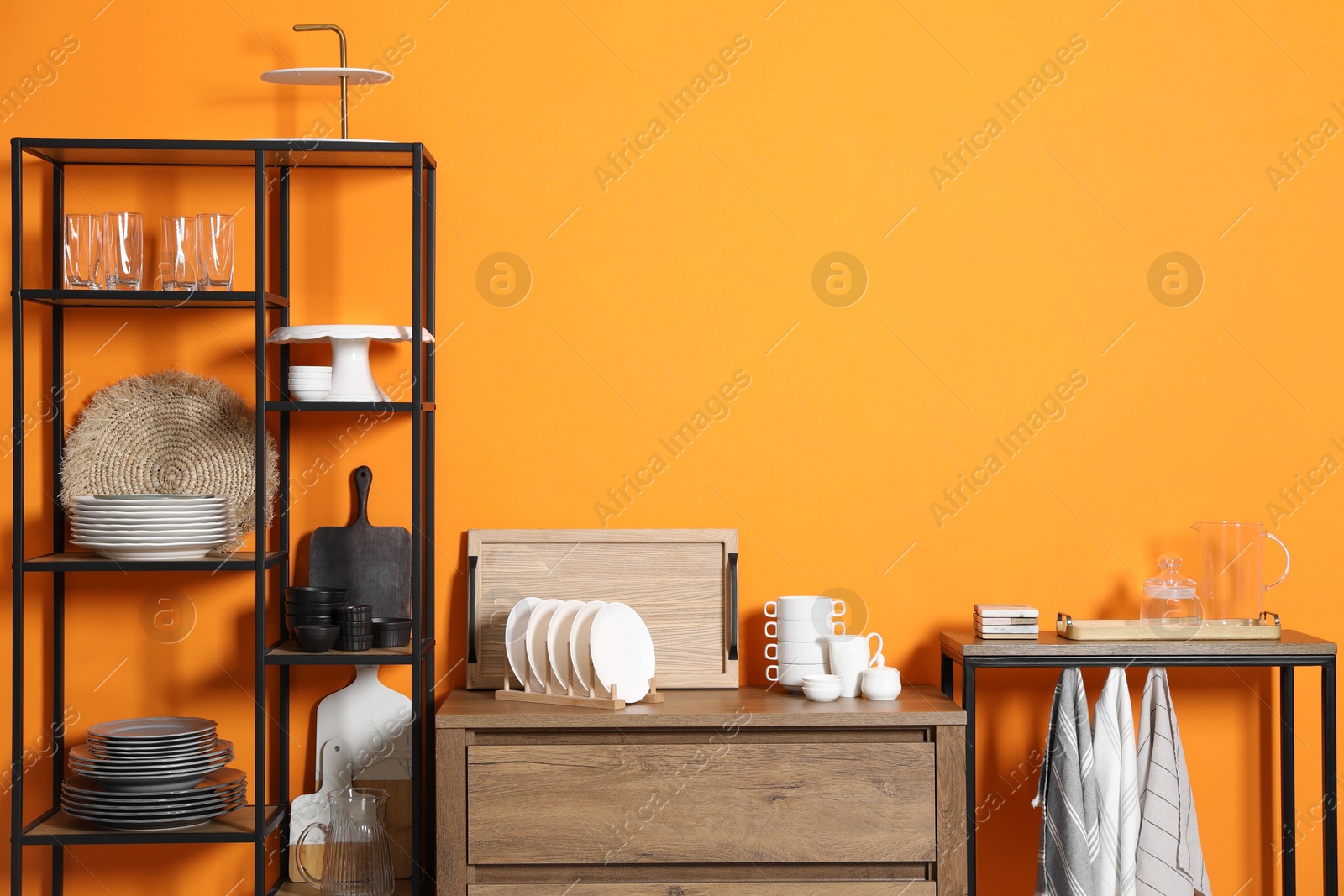 Photo of Storage stands and chest of drawers with kitchenware near orange wall indoors