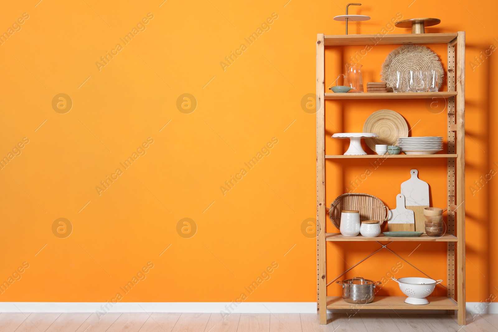 Photo of Wooden storage stand with kitchenware near orange wall indoors, space for text