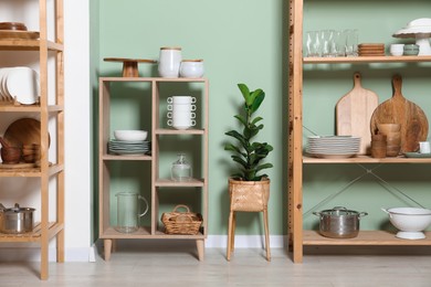 Photo of Wooden storage stands and shelving unit with kitchenware near green wall indoors