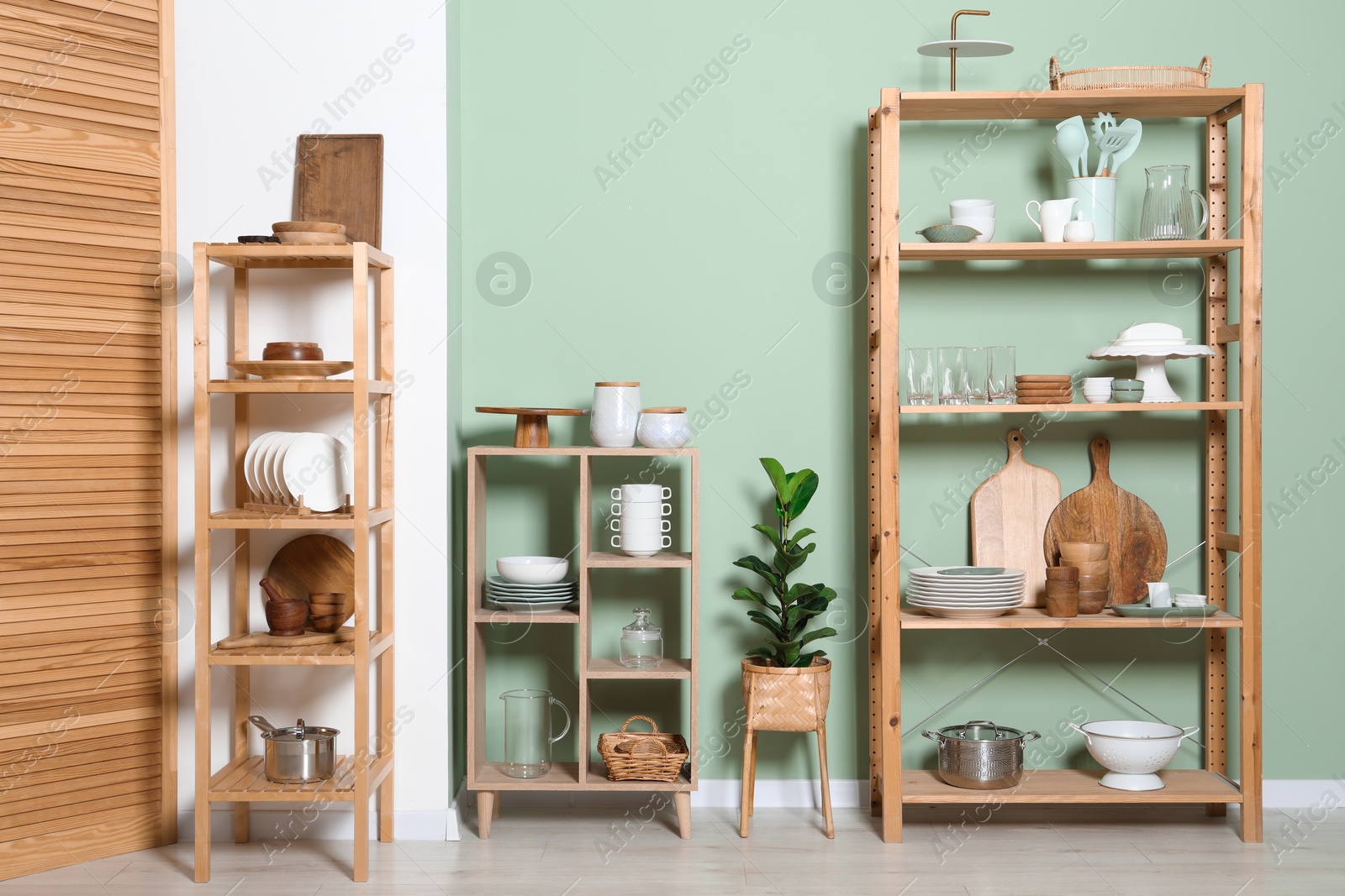 Photo of Wooden storage stands and shelving unit with kitchenware near green wall indoors