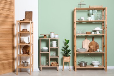 Wooden storage stands and shelving unit with kitchenware near green wall indoors