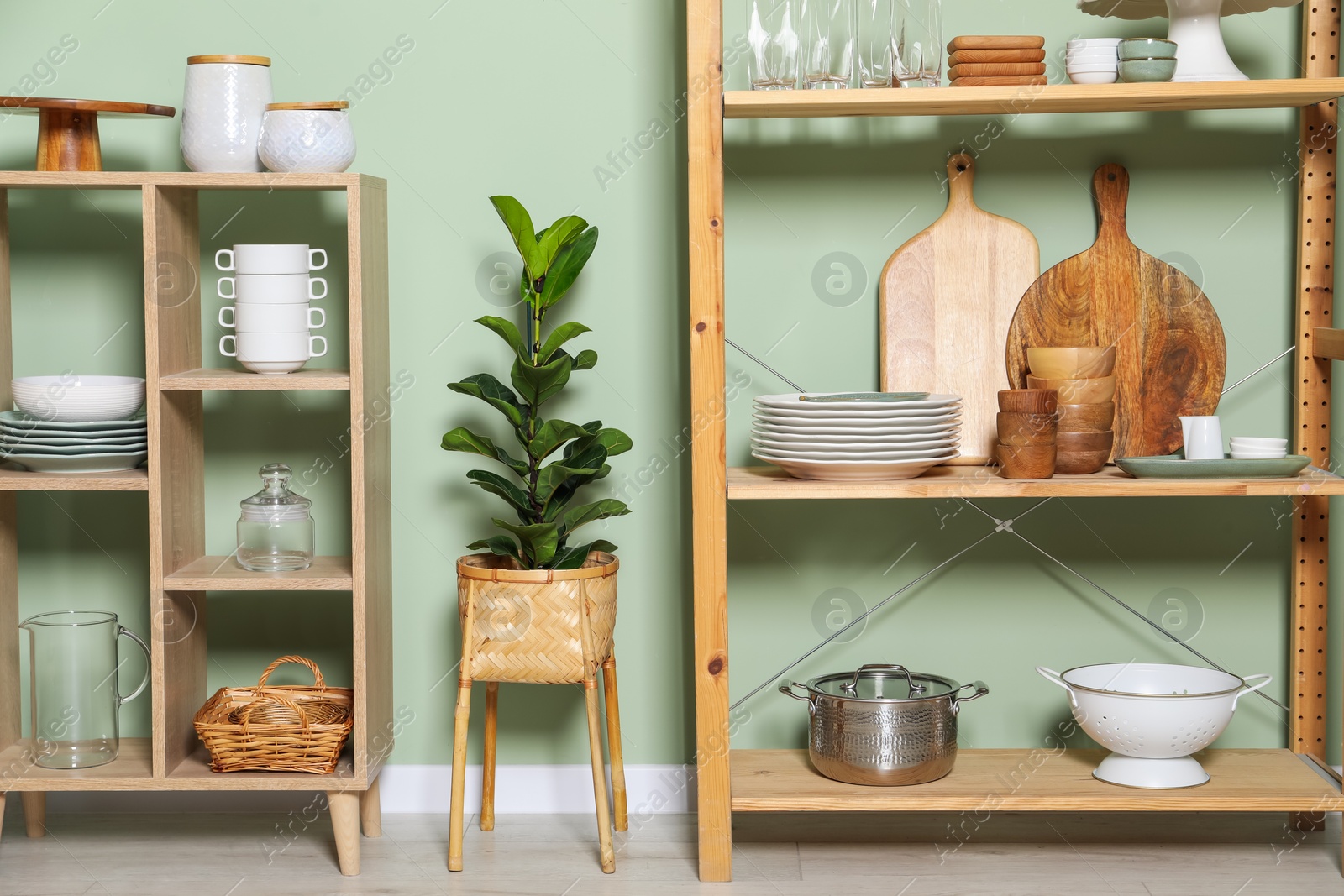 Photo of Wooden storage stand and shelving unit with kitchenware near green wall indoors