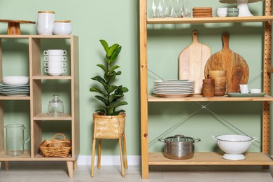 Wooden storage stand and shelving unit with kitchenware near green wall indoors