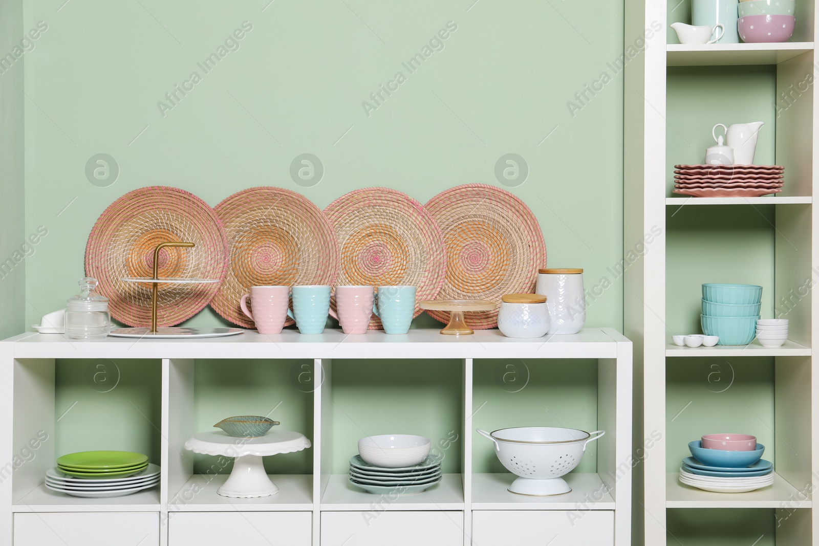 Photo of Shelving unit and storage cabinet with kitchenware near green wall