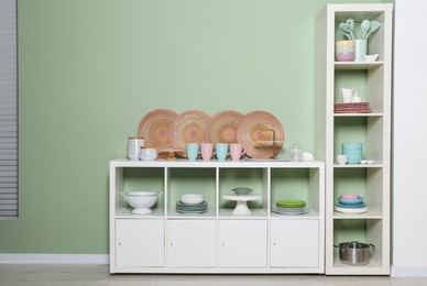 Shelving unit and storage cabinet with kitchenware near green wall