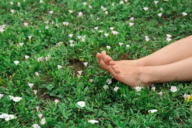 Photo of Woman sitting barefoot on green grass outdoors, closeup