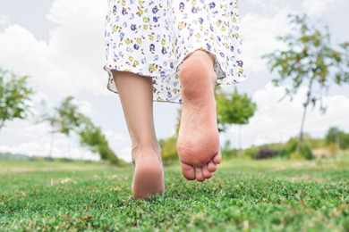 Photo of Woman walking barefoot on green grass outdoors, closeup