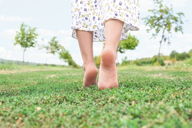 Photo of Woman walking barefoot on green grass outdoors, closeup