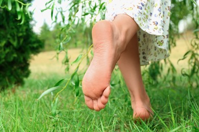 Photo of Woman walking barefoot on green grass outdoors, closeup