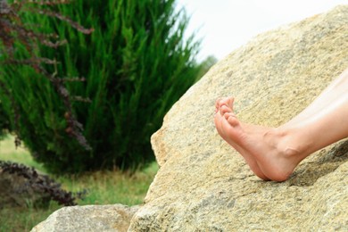 Photo of Woman sitting barefoot on rock outdoors, closeup