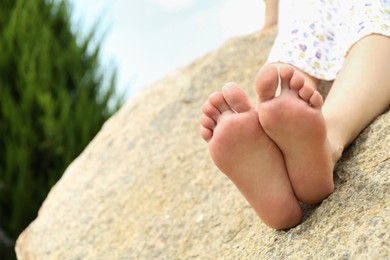 Photo of Woman sitting barefoot on rock outdoors, closeup