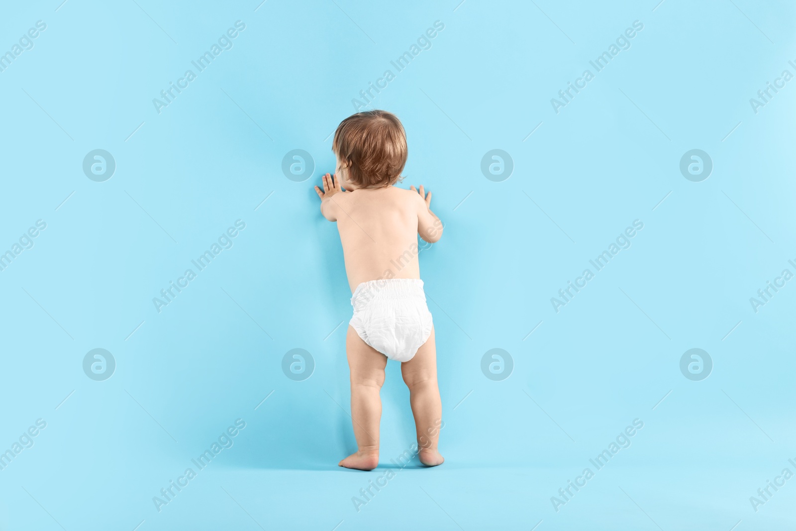 Photo of Little child in diaper on light blue background, back view