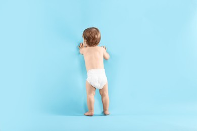 Photo of Little child in diaper on light blue background, back view