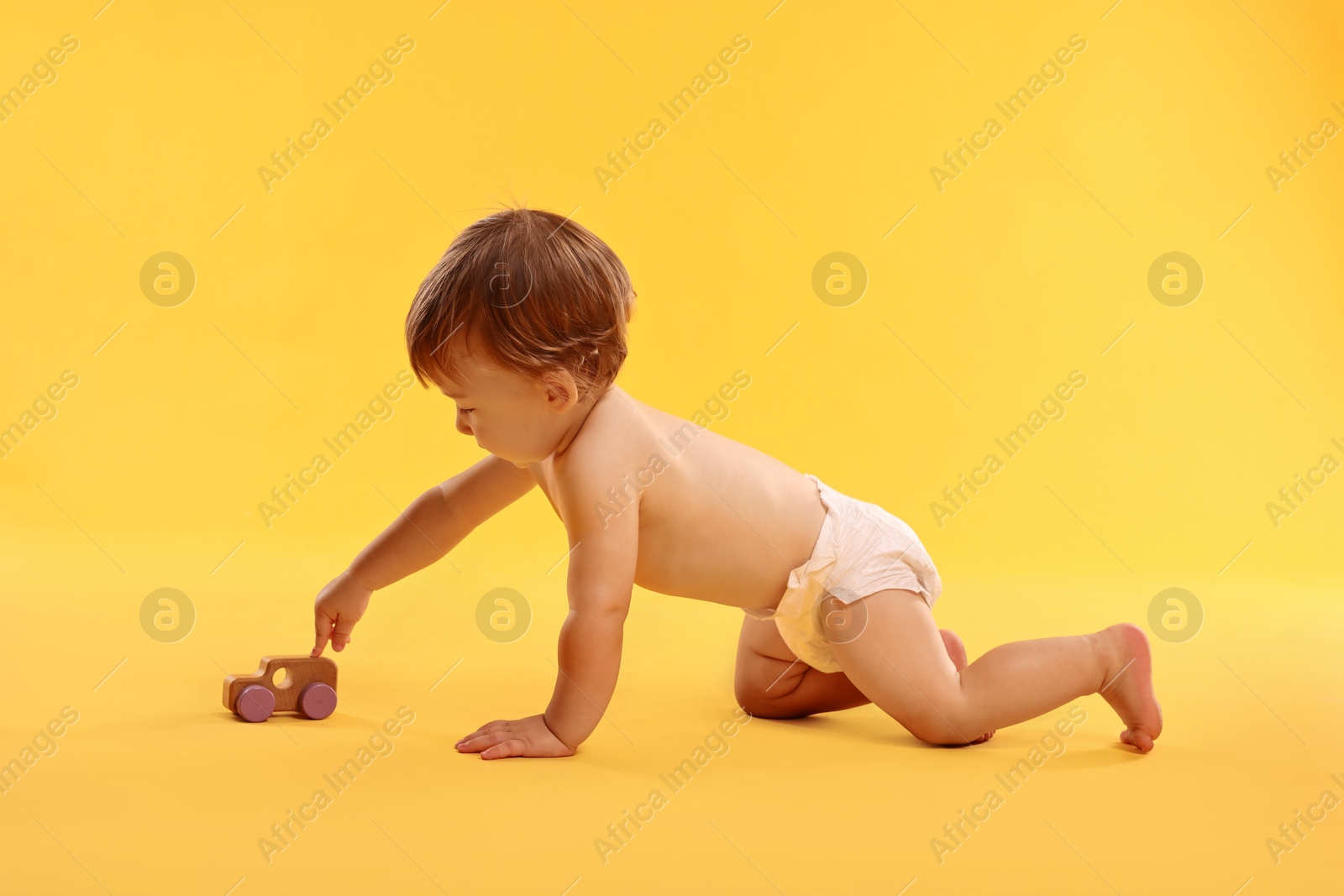 Photo of Little child in diaper with toy on orange background