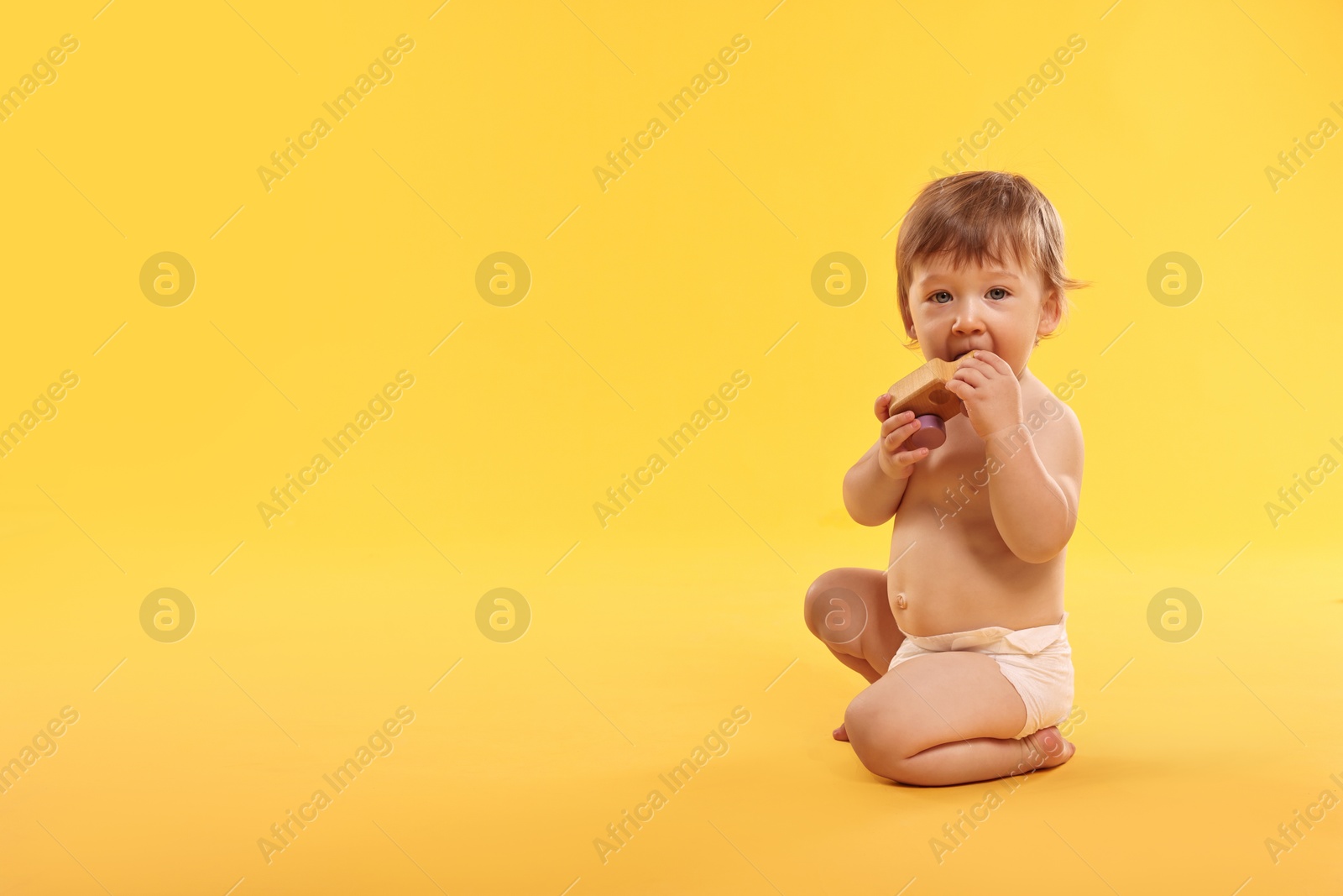 Photo of Little child in diaper with toy on orange background, space for text