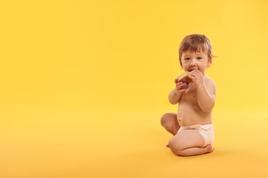 Photo of Little child in diaper with toy on orange background, space for text