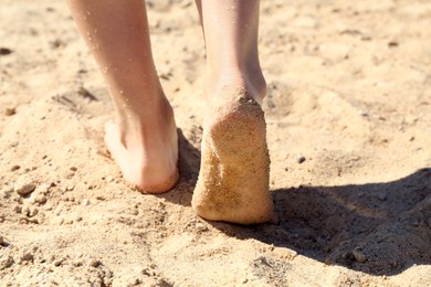 Photo of Woman walking barefoot on sand outdoors, closeup