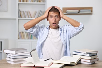 Photo of Overwhelmed student before exam at table among books indoors