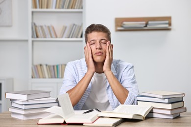 Overwhelmed student before exam at table among books indoors