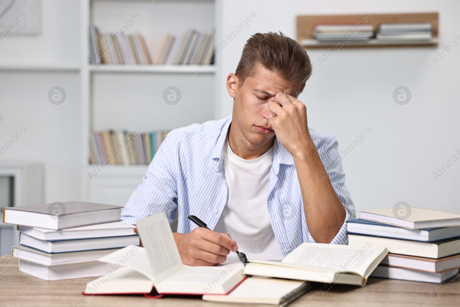 Photo of Tired student before exam at table among books indoors