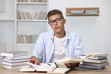 Tired student before exam at table among books indoors