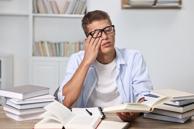 Tired student before exam at table among books indoors