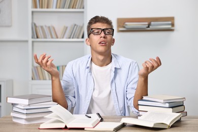 Tired student before exam at table among books indoors