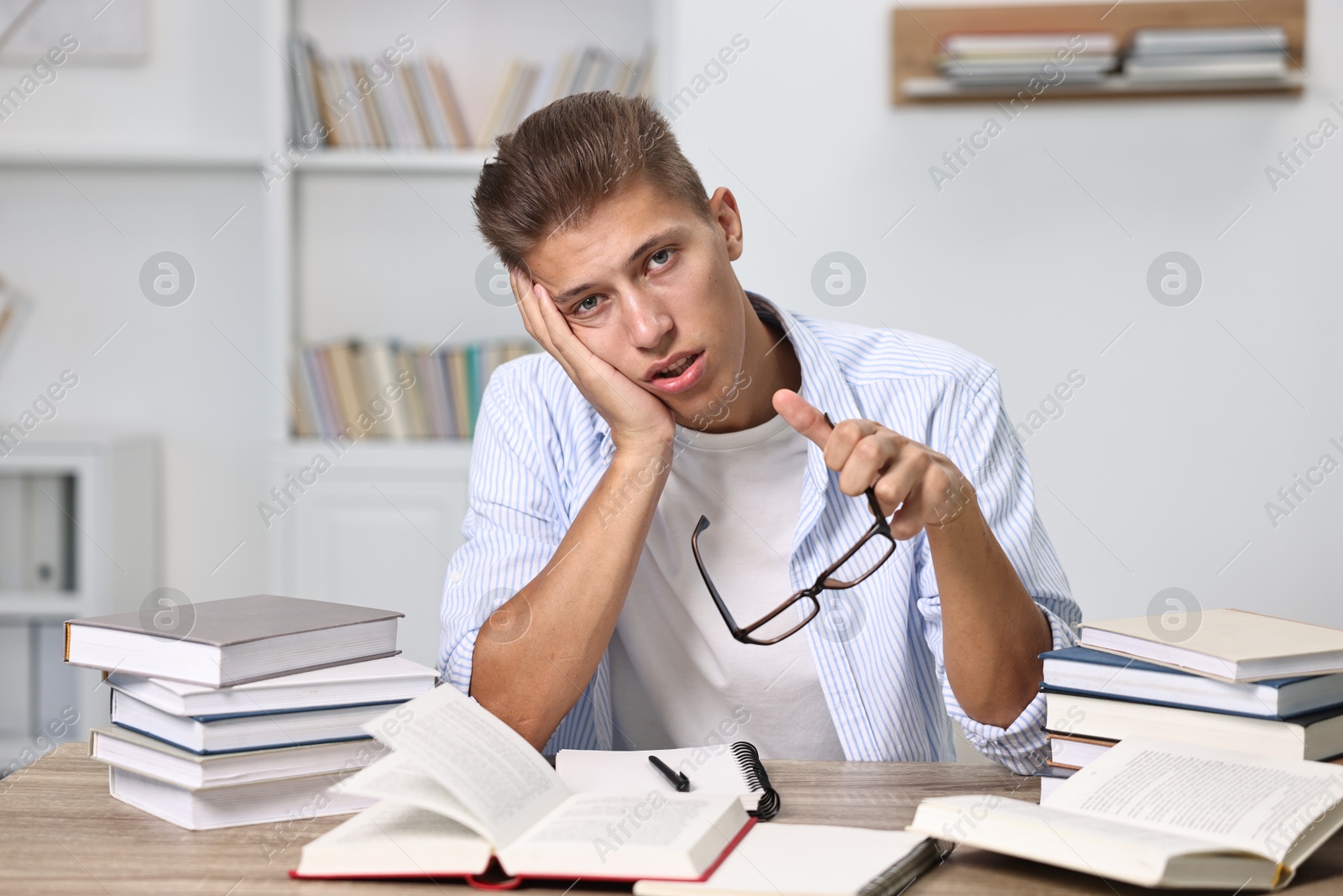 Photo of Tired student before exam at table among books indoors