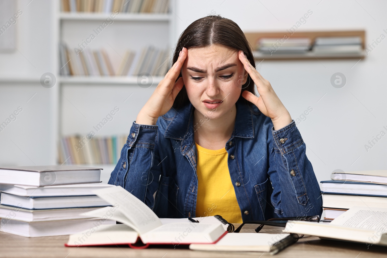 Photo of Tired student before exam at table among books indoors