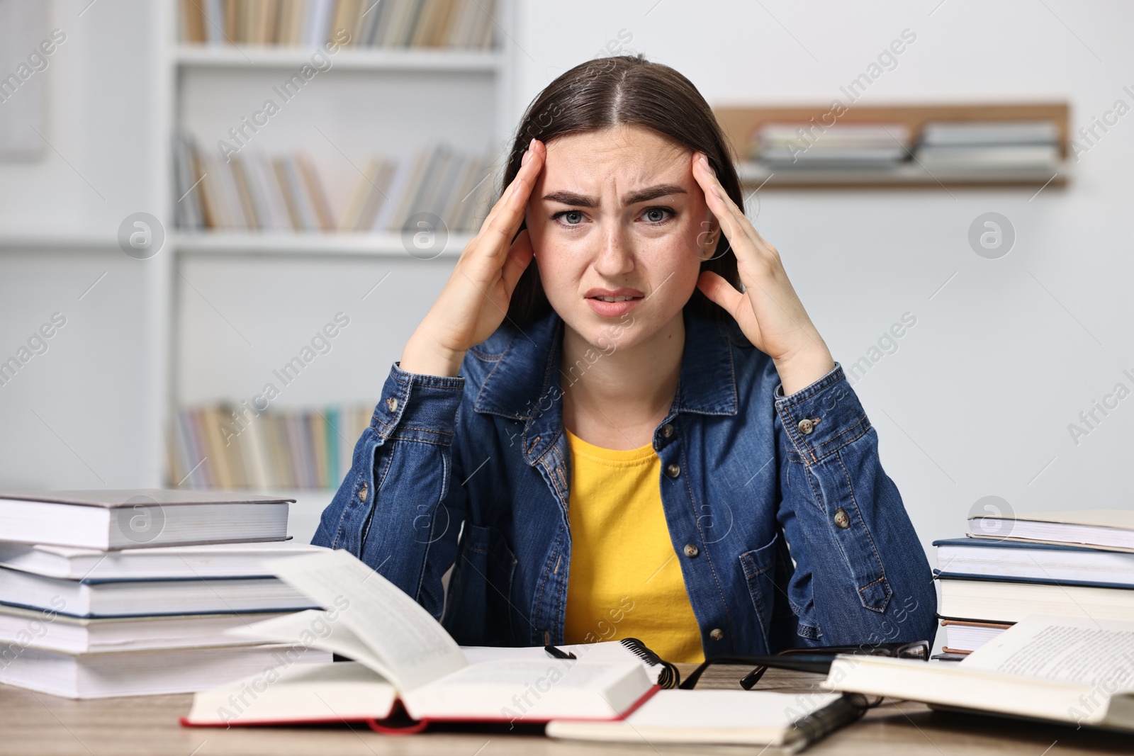 Photo of Overwhelmed student before exam at table among books indoors