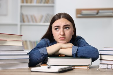 Overwhelmed student before exam at table among books indoors