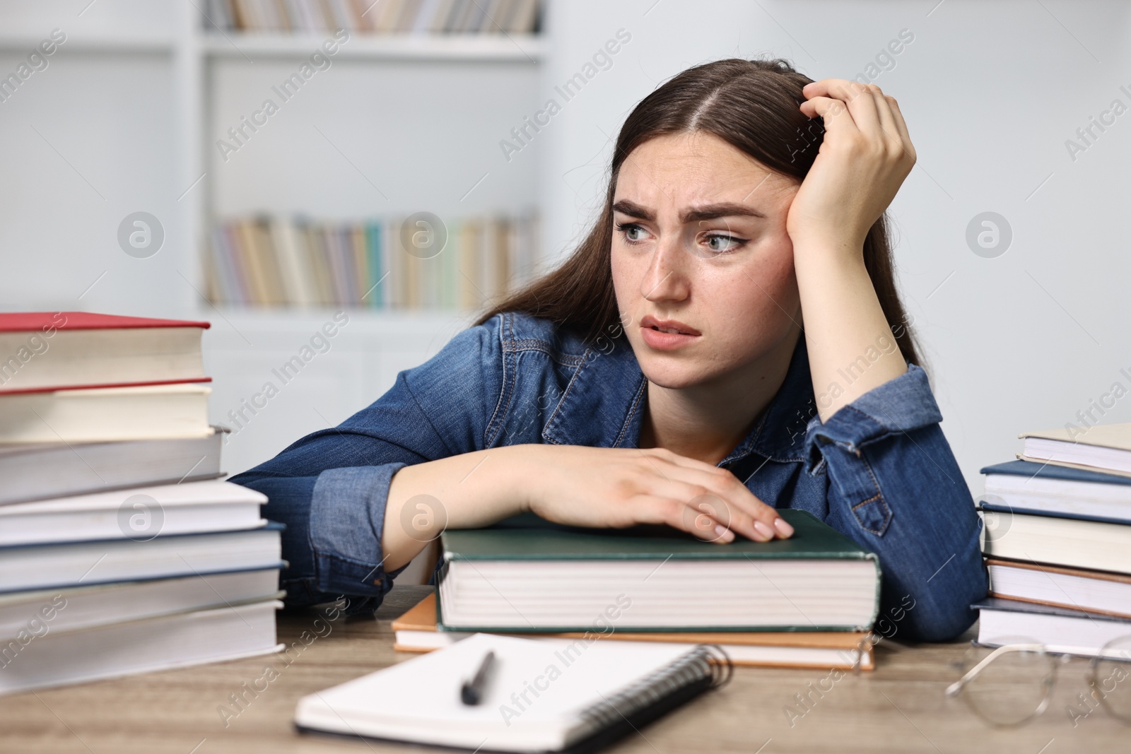 Photo of Overwhelmed student before exam at table among books indoors