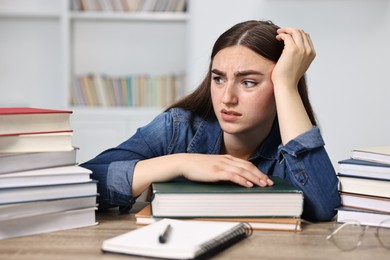 Overwhelmed student before exam at table among books indoors